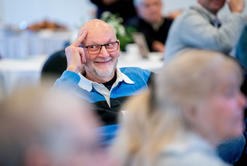 Man smiling, looking to the side, two fingers on his head